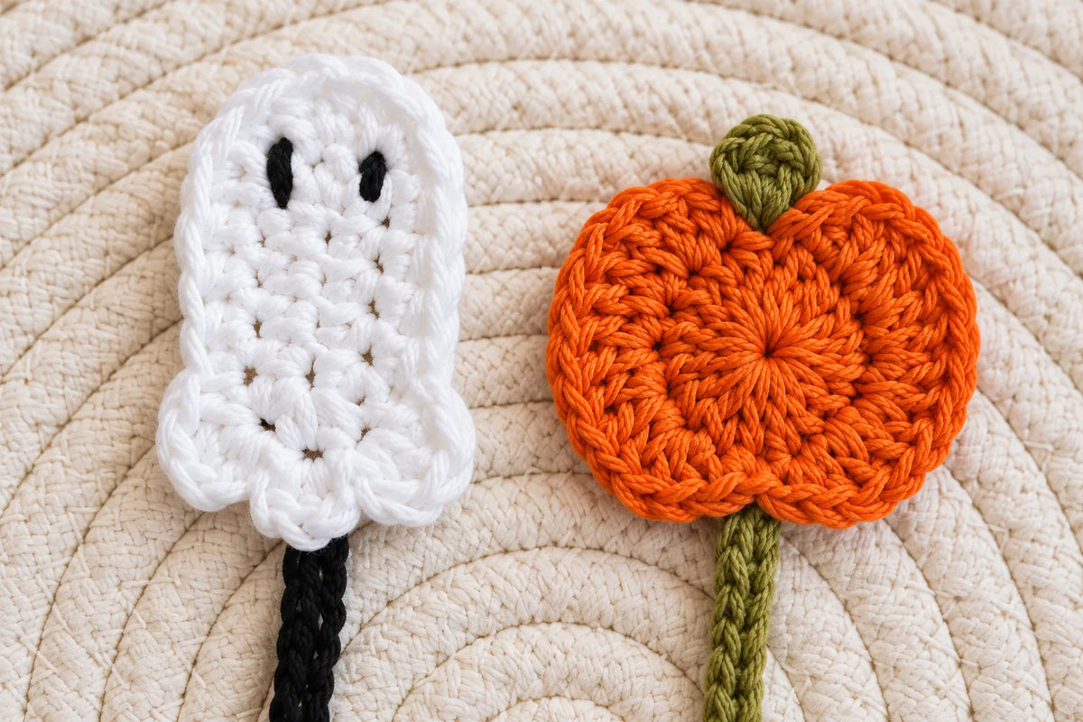 Primer plano de los dos marcapáginas tejidos a ganchillo: el fantasma blanco con los ojos bordados en negro y la calabaza naranja con el rabito verde