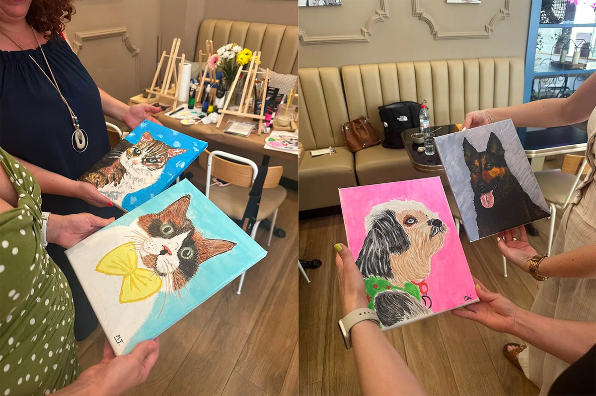 A la izquierda, dos participantes sostienen los retratos de gato que han pintado —uno atigrado sobre fondo azul y otro tricolor con un lazo amarillo—, con los caballetes y las flores de la mesa de trabajo al fondo; a la derecha, otras dos sostienen un perrito blanco y negro sobre fondo rosa y un perro negro y fuego sobre fondo gris